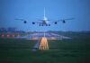 An airplane approaching the runway at night with landing lights illuminated