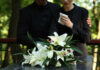 Mourners in black holding white flowers at funeral