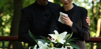 Mourners in black holding white flowers at funeral