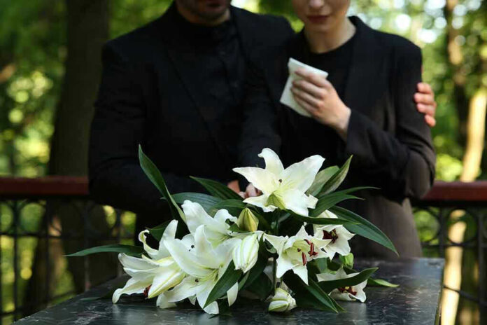 2314885229 Mourners in black holding white flowers at funeral