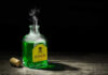 Green poison bottle with cork on wooden surface.