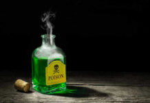 Green poison bottle with cork on wooden surface.