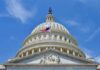 The U.S. Capitol building with an American flag flying in front against a blue sky