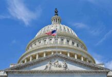 The U.S. Capitol building with an American flag flying in front against a blue sky