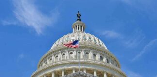 The U.S. Capitol building with an American flag flying in front against a blue sky