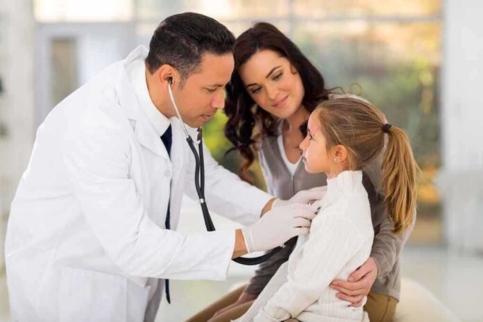 A doctor examines a young girl with a stethoscope while her mother watches