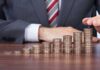 Businessman stacking coins in ascending order on a wooden table