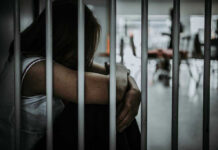 Prison Becomes HUNTING Ground — Feds Knew Person sitting behind bars with arms wrapped around knees.
