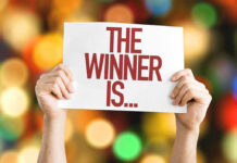 Hands holding a sign reading The Winner Is...