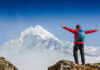 Hiker with arms outstretched in front of snowy mountains.
