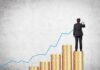 Businessman standing on stacks of coins, drawing a growth chart