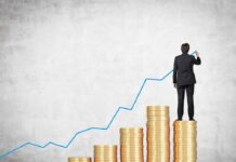 Businessman standing on stacks of coins, drawing a growth chart
