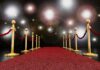 A red carpet lined with gold stanchions and ropes under bright spotlights