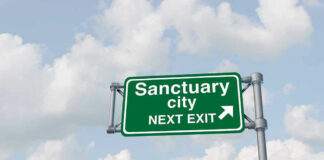 Green road sign saying sanctuary city next exit