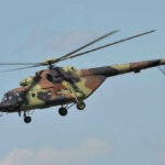 Camouflage military helicopter in flight against blue sky.