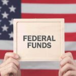 Person holding a sign that reads FEDERAL FUNDS in front of an American flag