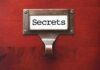 Metal label holder saying Secrets on wood background
