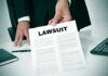 Person holding a document titled LAWSUIT in office.