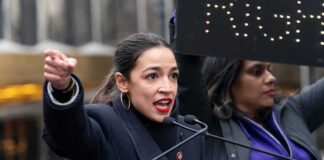 A woman passionately speaking at a political rally with a sign in the background