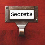 Metal label holder saying Secrets on wood background