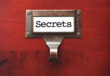 Metal label holder saying Secrets on wood background