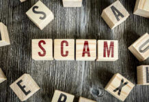 Wooden blocks spell SCAM on a rustic surface.