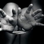 Two hands reaching out, bound by rope in a black and white image