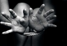 Two hands reaching out, bound by rope in a black and white image