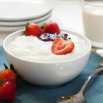 A bowl of creamy dessert topped with fresh strawberries and a drizzle of jam