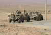 Soldiers beside military vehicles in a desert area.