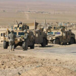 Soldiers beside military vehicles in a desert area.