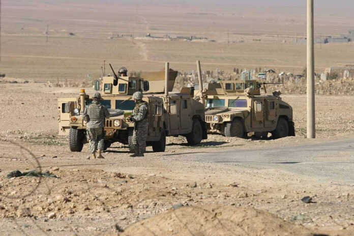 Soldiers beside military vehicles in a desert area.