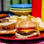 A plate with a hamburger, hot dog, and potato chips on a picnic table