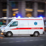 Nun Attack in Jerusalem—Shocking BRUTALITY Ambulance driving on urban street with lights flashing.