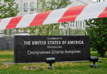 U.S. Embassy sign behind red-and-white caution tape.