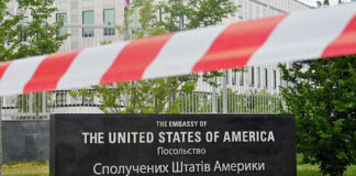 U.S. Embassy sign behind red-and-white caution tape.