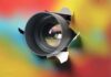Camera lens emerging through torn colorful paper