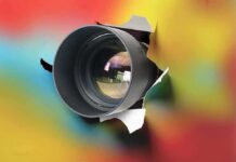 Camera lens emerging through torn colorful paper