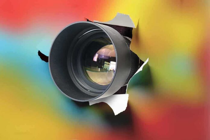 shutterstock_1892209375-2- Camera lens emerging through torn colorful paper