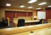 CHILLING — LENIENT Judge PROMOTED to LEAD Domestic-Violence COURT! Interior view of an empty courtroom with wooden furniture and American flags
