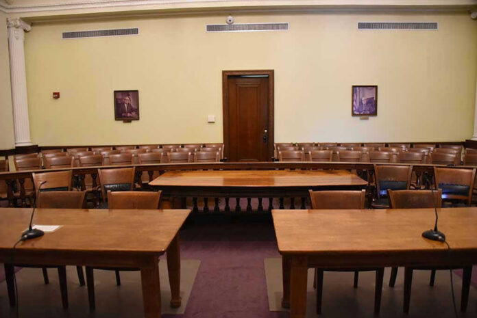 1291095706-2 Empty courtroom with wooden tables, chairs, and a door.