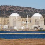 Big Green: Trump Unleashes Billion Nuclear Revival Nuclear power plant with domed structures beside a water body and mountains in the background