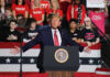 Politician speaking at rally with supporters behind him.