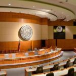 Massive Crypto Haul—Congress Smells Smoke Interior view of a government chamber with wooden paneling and seating