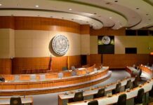 Massive Crypto Haul—Congress Smells Smoke Interior view of a government chamber with wooden paneling and seating