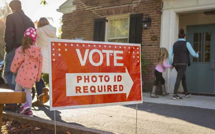 shutterstock_512254585 Red voting sign with arrow near people entering a polling place