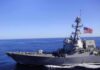 Naval destroyer sailing on open sea with flag flying