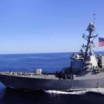 Naval destroyer sailing on open sea with flag flying