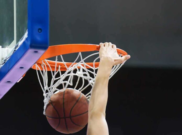 shutterstock_1448640140 Basketball player dunks ball through orange rim