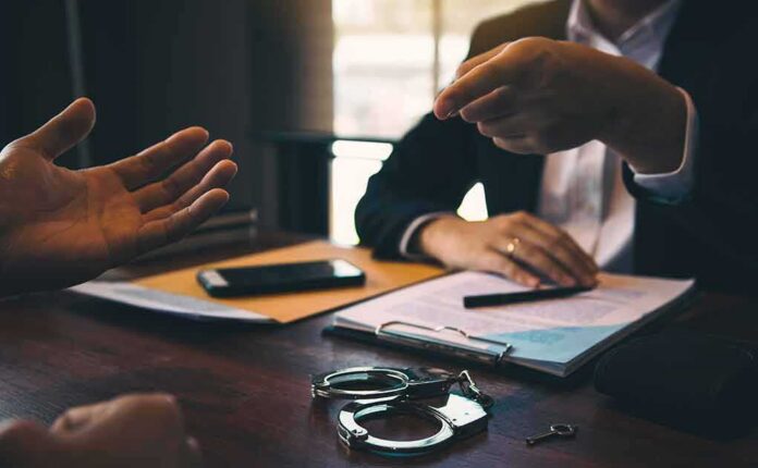 Two people in discussion at a desk with handcuffs and documents